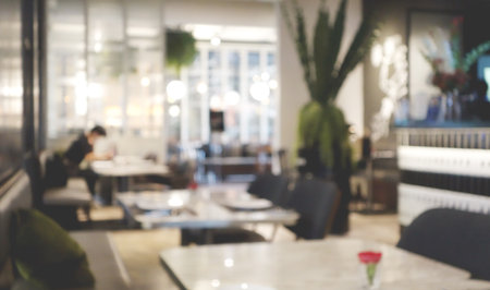 Blurred abstract background of cafe or restaurant. Indoor cafe with tables and chairs. Street cafe in the evening in modern terrace. Customers sit at tables in a terrace area.の写真素材