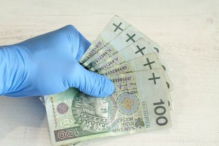 Human hand in a blue protective glove holding a bundle of banknotes.