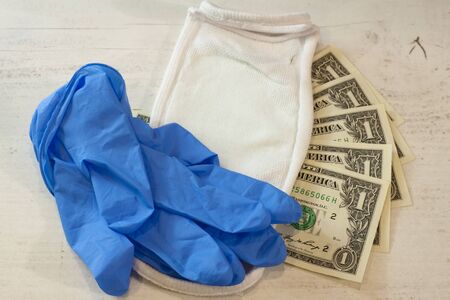 Human hand in a blue protective glove holding a bundle of banknotes and protective mask.