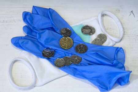 Human hand in a blue protective glove with a protective face mask lying down and scattered coins.