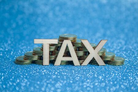 Pyramid of piles of gold coins on a blue background and the words tax.の写真素材