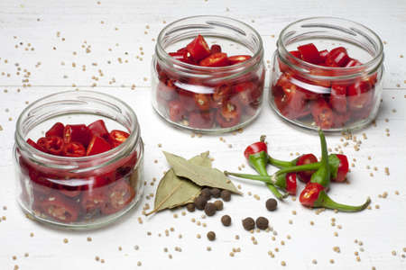 Chillies, cut and placed in jars, waiting to be marinated. On a white table with tails of peppers and spices used for pickling.の写真素材