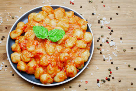 Traditional homemade Italian gnocchi in aromatic tomato sauce served on a decorative plate and garnished with herbs, basil, colored pepper, garlic and pink Himalayan salt.の写真素材