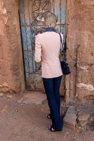 A Western female tourist standing at the old metal door in Ushaiqer Heritage Village, Saudi Arabia. Back view.の写真素材