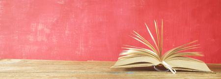opened book on red grungy background, panoramic, good copy space, reading learning, literature concept.の写真素材