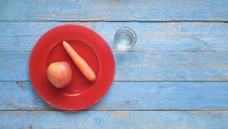 Apple and carrot on a red plate and glass of water, dieting, healthy nutrition, fitness concept, flat layの写真素材