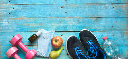 work out in times of coronavirus; corona mask, disinfectant spray, pair of runners, dumbbells, water, apple, pear, coronavirus policies conceptの写真素材