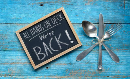 Restaurant announcing reopening after the corona lockdown on black board, cutlery on rustic table,...