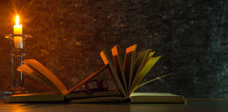 Open book, hardback books and a candle, dim light. Education,reading,literature concept. Good copy space.の写真素材