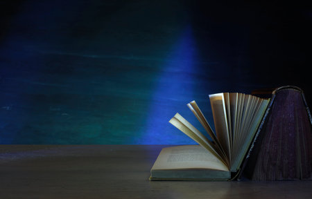 Open book, hardback book on wooden table on dark background. Home office,back to school,education,reading. Copy space,negative space technique.の写真素材