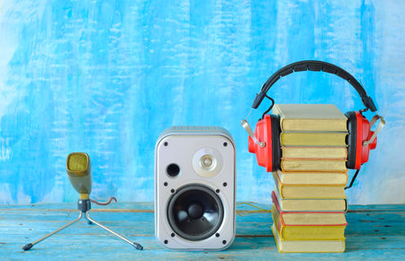 audio book concept with stack of books and vintage headphones,loudspeaker and old microphone, blue,...