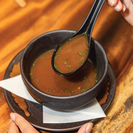 A woman's hand holds a spoon with soup on a wooden backgroundの写真素材