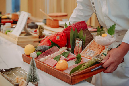Japanese chef holding a wooden tray with sashimi and sushi rollsの写真素材