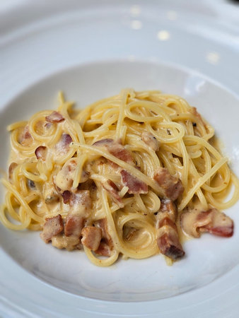 Spaghetti Carbonara with bacon on a white plate in a restaurantの写真素材