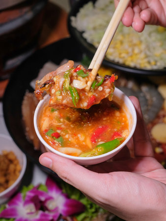 Close-up of a woman's hand holding a bowl of spicy stir-fried pork with chopsticks