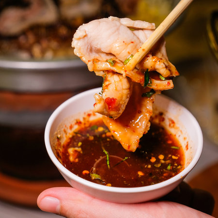 chopsticks picking up grilled chicken in a bowl with spicy sauce