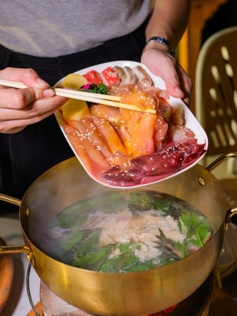 Hands of a woman in a restaurant serving a hot pot with meatの写真素材