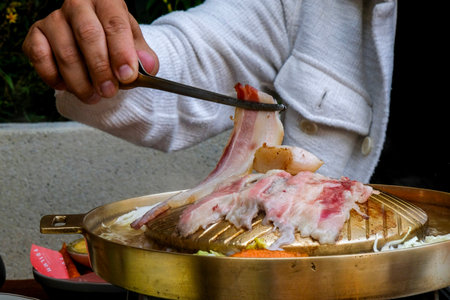 Close-up of a man's hand holding a knife and cutting bacon on a hot potの写真素材