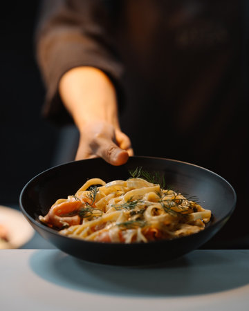 Close-up of female hands holding black bowl with tasty pasta.の写真素材