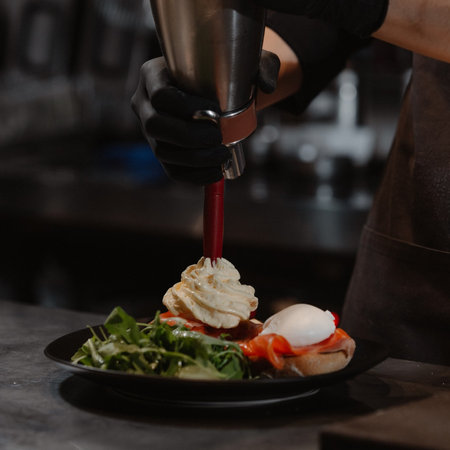 Close-up of a barman's hand in black gloves pouring cheese from a shaker into a cup of saladの写真素材