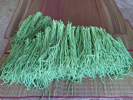 a large pile of green beans on woven bamboo mats, likely freshly harvested.