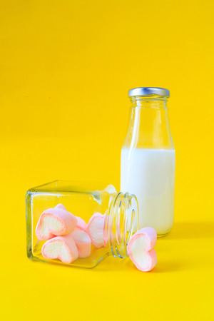 Heart shape marshmallow with milk bottle on yellow backgroundの写真素材