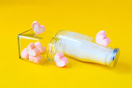 Heart shape marshmallow with milk bottle on yellow backgroundの写真素材