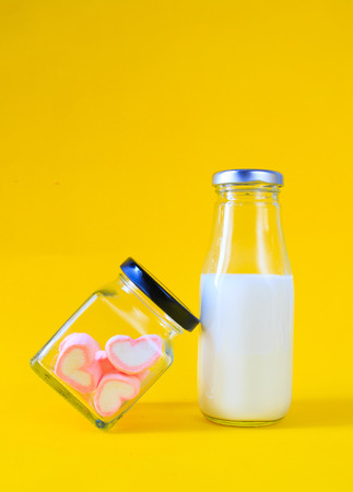 Heart shape marshmallow with milk bottle on yellow backgroundの写真素材
