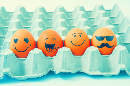 four brown eggs  with faces drawn  arranged in cartonの写真素材