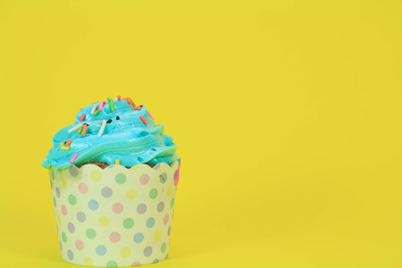 Blue Cupcake with colorful candy on yellow backgroundの写真素材