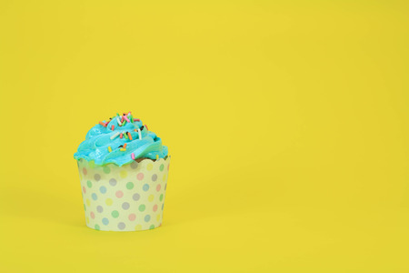 Blue Cupcake with colorful candy on yellow backgroundの写真素材