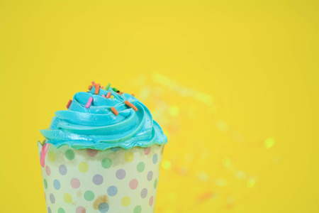 Blue Cupcake with colorful candy on yellow backgroundの写真素材