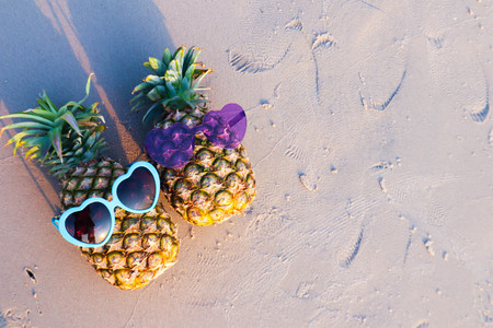 Couple of pineapples in funny sunglasses on the sand in sunset. Tropical summer vacation concept.の写真素材