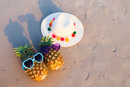 Pineapple fruit in sunglasses with hat on the sand.の写真素材