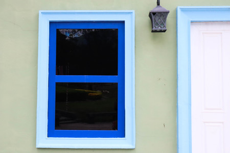 Blue window glass on green wall of house.の写真素材