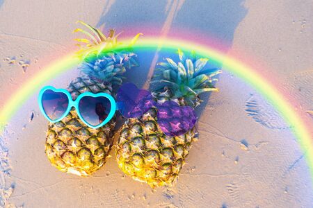 Couple of pineapples in funny sunglasses on the sand in sunset. Tropical summer vacation concept.の写真素材