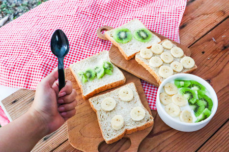 Women Holding spoon with wholegrain bread slices with banana,kiwi and banana bowl with yogurt.の写真素材