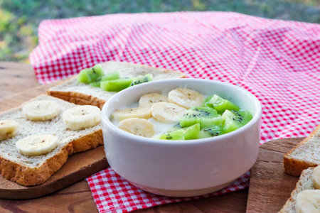 Tropical fruit kiwi, banana bowl with yogurt and Wholegrain bread slices with banana,kiwi on wooden table.の写真素材