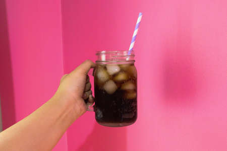 Woman's hand holding cola cool in a glass of water on pink background.の写真素材