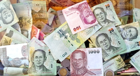 Various Thai bank notes and coins in transparent donation box in thai templeの写真素材