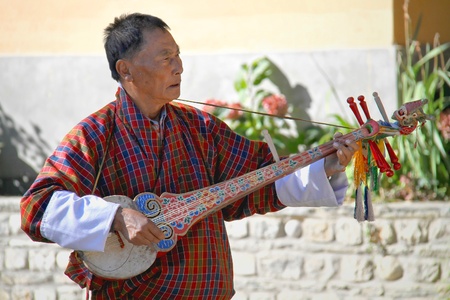 PARO, BHUTAN - November10, 2012 : Unidentified old man musician in traditional dress (Gho) playing Dramnyen instrument at hotel in Paro, Bhutanのeditorial素材