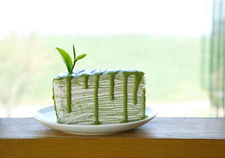 Piece of green tea crape cake on white plate and decorated with fresh tea leafの写真素材