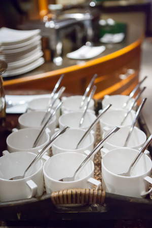 rows of pure white cup and saucer with teaspoon, reflection on tableの写真素材