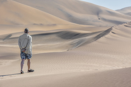 A tourist walking and contemplating in the sand dunes near the coastal towns of Swakopmund and Walvisbay at the Atlantic Ocean in Namibia Southern Africa looking into the distanceの写真素材