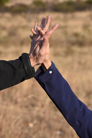 Two hands holding each other crossing fingers in the air symbolizing connection and friendship with black and blue sleevesの写真素材