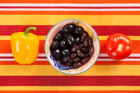 Healthy food on the table covered with a tablecloth with stripes in the garden. Yellow peppers and red tomatoes rich in vitamins are a very good choice for a healthy diet. Olives are the best source of omega-3. gifts of summer, pleasing to the eyeの写真素材