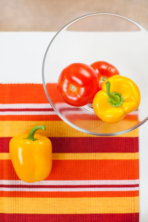 Healthy vegetables on the table covered with a tablecloth with stripes in the garden. Yellow peppers and red tomatoes rich in vitamins are a very good choice for a healthy diet. Natural light and good mood.の写真素材