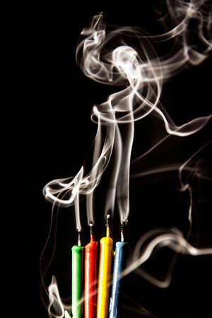 Green, red, yellow and blue birthday candles that have been blown out and billowing smoke. Shot against a black background.の写真素材