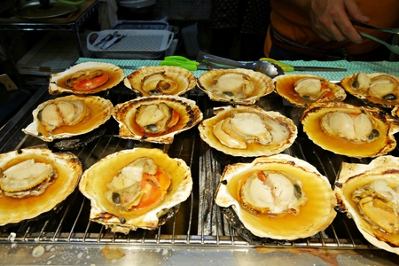 Sizzling grilled fresh Hotate (Japanese Scallop) on shells over a stove at the morning market in...