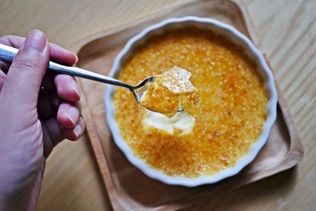 A hand of woman cracked through a crunchy top layer of a Creme brulee, burnt cream, crema catalana or Trinity cream, a rich and velvety custard base topped with a contrasting layer of hard caramel. Top view.の写真素材